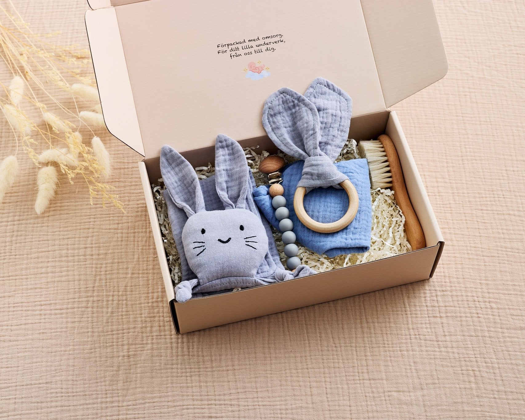 Blått babyset i presentförpackning med snuttefilt formad som en kanin, bitring med tygöron, träborste, napphållare med träpärlor och en haklapp i 100% bomull. Perfekt för nyfödda och babyshowers.