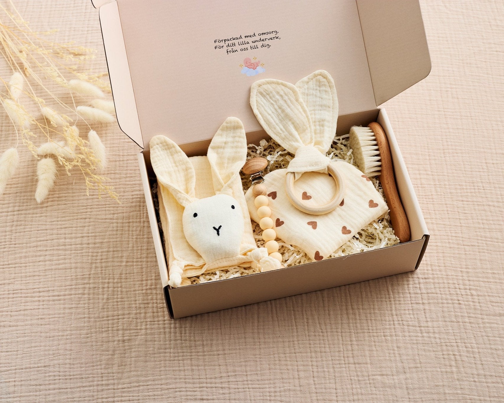 Beige babyset i presentförpackning med snuttefilt formad som en kanin, bitring med tygöron, träborste, napphållare med träpärlor och en haklapp med hjärtmönster. Perfekt för nyfödda och baby showers.